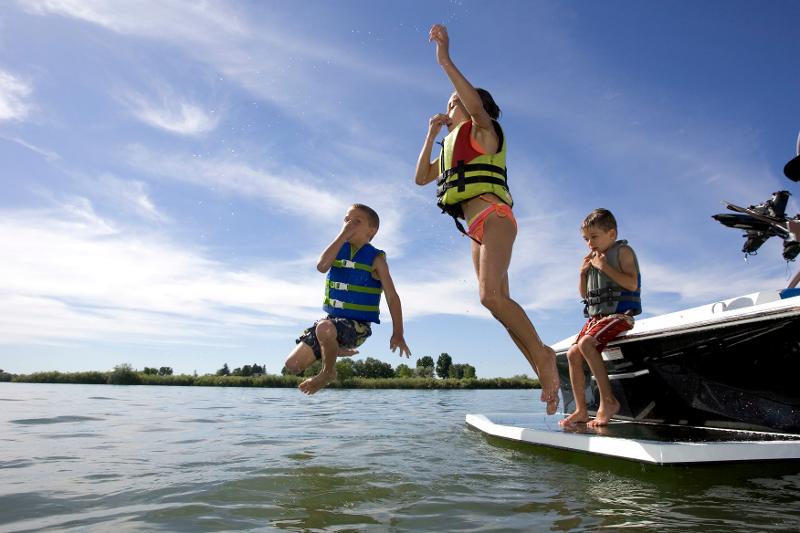 Kinder mit Schwimmwesten springen von Boot ins Wasser im Sommercamp Bodensee