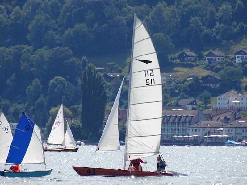 Mehrere Segelboote fahren auf einem See mit den Bergen im Hintergrund im Segelcamp