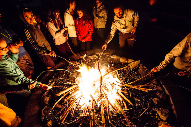 Ein paar Schüler:innen genießen gemeinsam ein Lagerfeuer mit Stockbrot