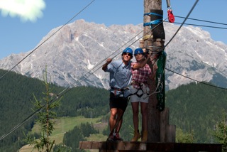 Zwei Jugendliche stehen im Kletterpark zwischen den Baumwipfeln vor einem schönen Bergpanorama im Ferienlager Aargau.