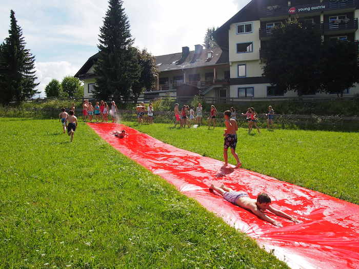 Teilnehmer eines Englisch Sommercamps haben Spass auf einer roten Wasserutsche im Garten