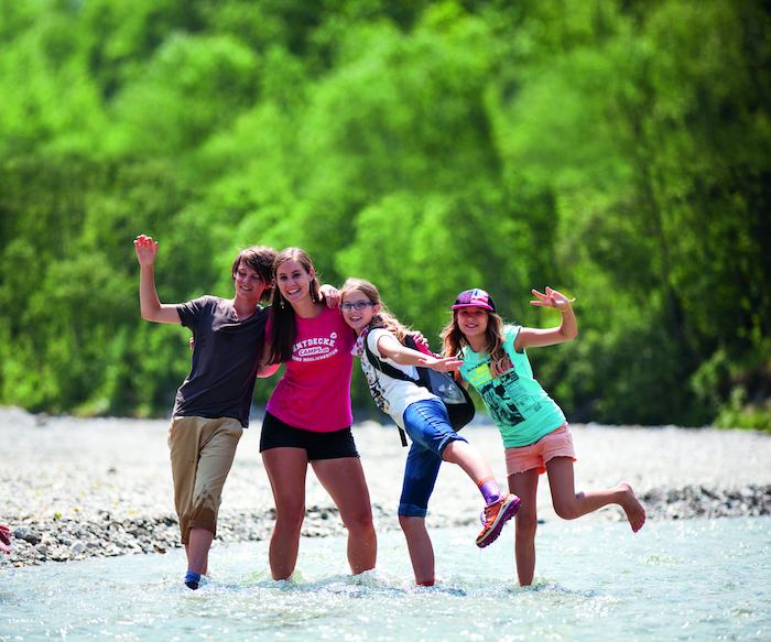 Eine Betreuerin und drei Kinder stehen bis zu den Knöcheln in einem Fluss und lächeln