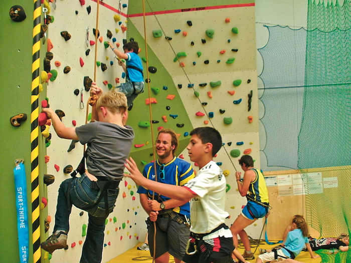 Im Camp für Kinder klettern die Teilnehmer mit Sicherung an einer Indoor-Kletterwand hinauf