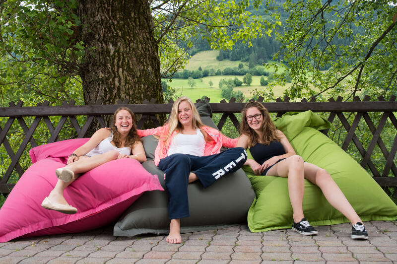 Drei Mädchen sitzen während ihres Englisch-Camps Schweiz auf Sitzsäcken im Garten und haben Spaß 