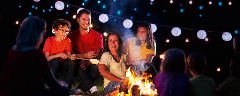Erlebt zusammen als Familie tolle Momente beim Lagerfeuer Eine Familie macht sich Stockbrot und sitzt gemeinsam beim Lagerfeuer