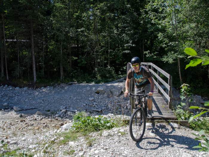 Ein Junge fährt mit dem Fahrrad über eine Brücke im Ferienlager in den Alpen