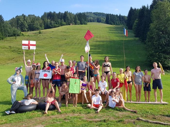 Kinder und Jugendliche stehen vor einem Hang und halten verschiedene Flaggen.