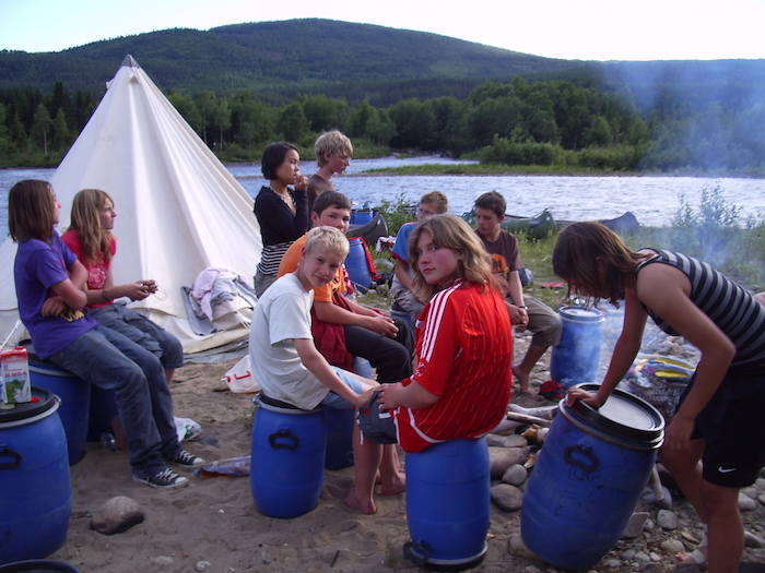 Eine Gruppe Kinder vom Kanu-Camp sitzt in einem Kreis neben den Zelten am Flussufer.