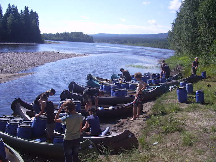 Eine Gruppe Jugendliche vom Kanu-Camp steht mit den Kanus am Flussufer.