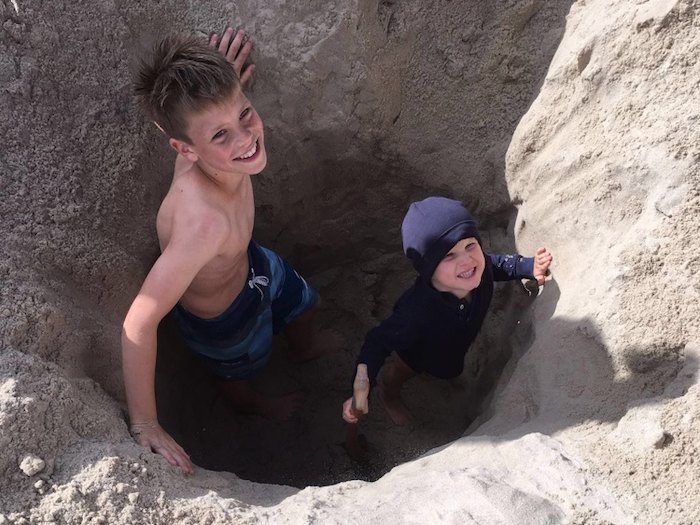 Zwei Jungs buddeln ein Loch im Sand im Surfcamp