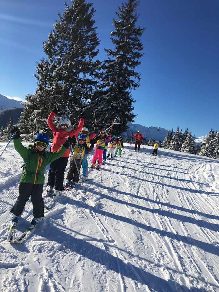 Kinder vom Skilager Österreich stehen auf der Piste und halten ihre Stöcke nach oben