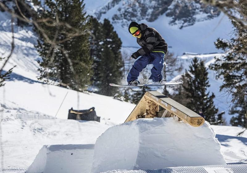 Ein Junge macht einen Trick auf dem Snowboard im Ferienlager Graubünden