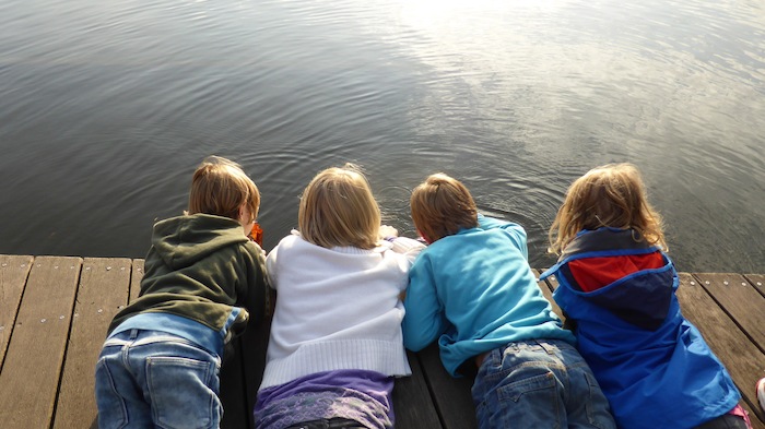 Drei Kinder liegen auf einem Steg und schauen ins Wasser