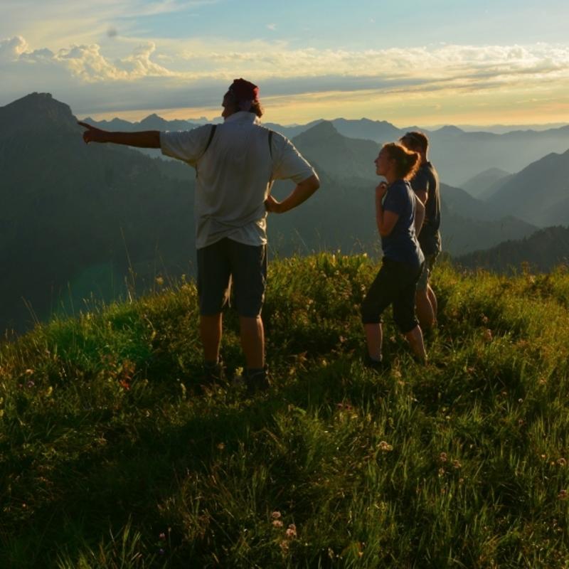 Ein Mann zeigt zwei Kindern den Weg im Ferienlager in den Alpen