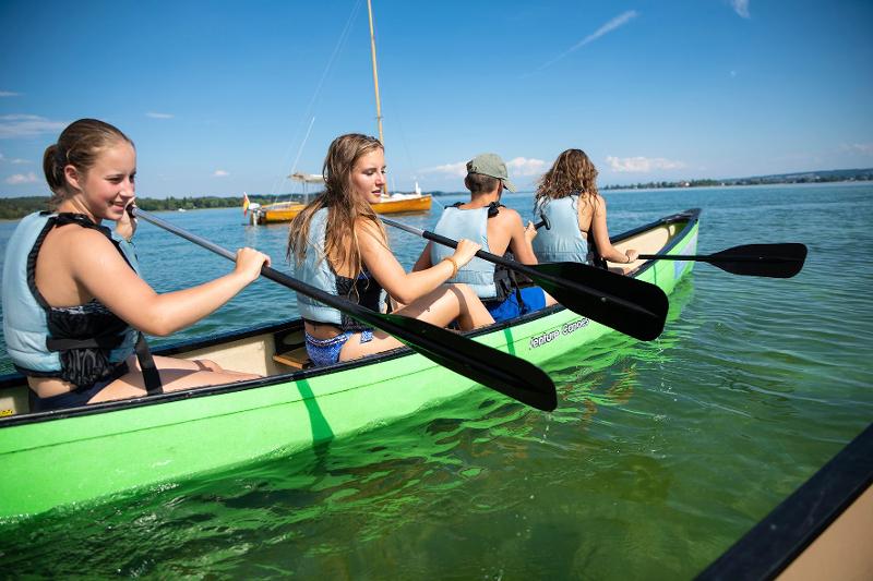 Teilnehmer eines Sprachcamps fahren in grünem Kanu auf dem Bodensee