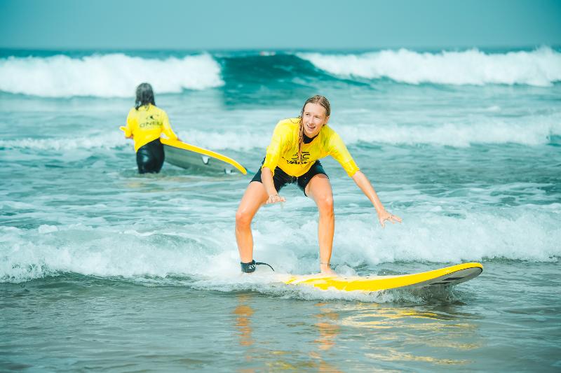 Eine Jugendliche lernt gerade am Strand bei ihrem Surftraining wie sie sicher auf dem Surfbrett steht