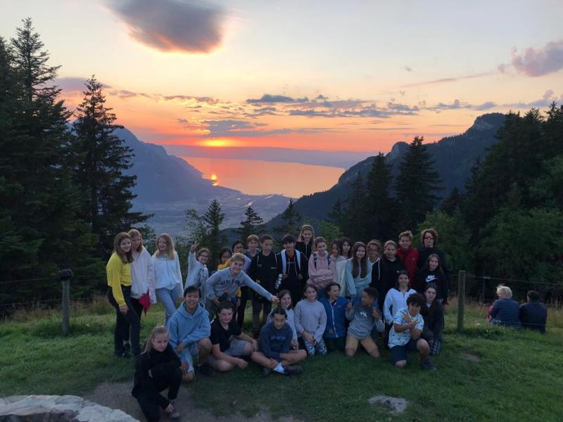 Teilnehmer eines Englischcamps stehen in einer Gruppe auf einem Berg und hinter ihnen geht die Sonne unter