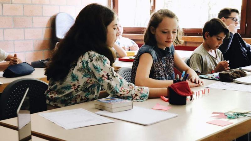 Mädchen sitzen an einem Tisch auf dem Stifte und Bücher liegen und lernen etwas spannendes während ihres Ferienlerncamps