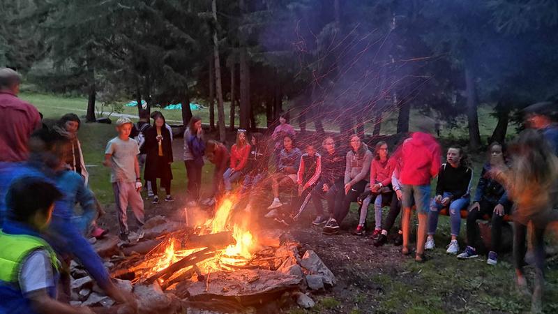 Teilnehmer einer Sprachreise Französisch Schweiz sitzen in der Dämmerung am Lagerfeuer