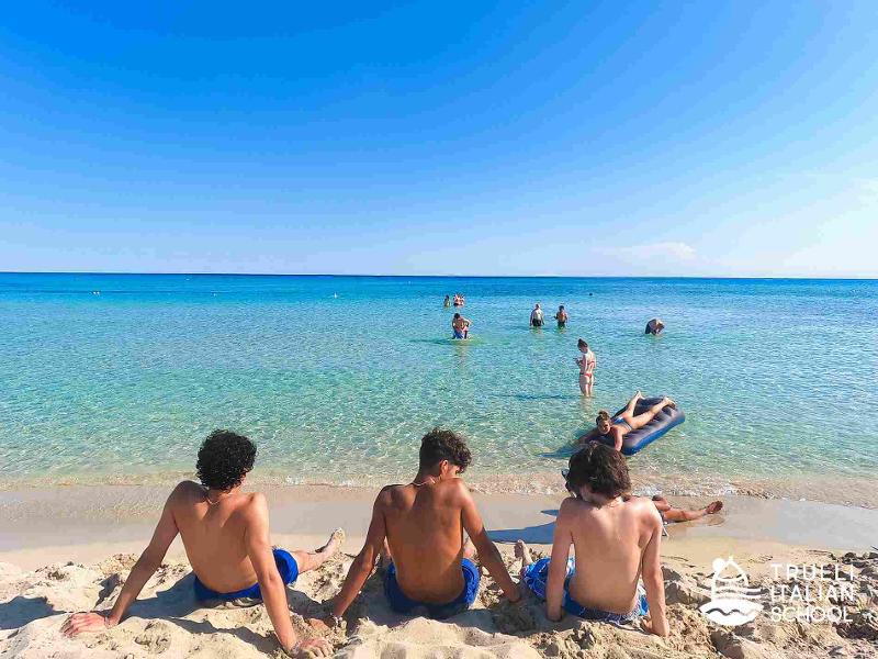 Ein kleines Grüppchen sitzt gemeinsam am Strand Italiens und blickt auf das Meer
