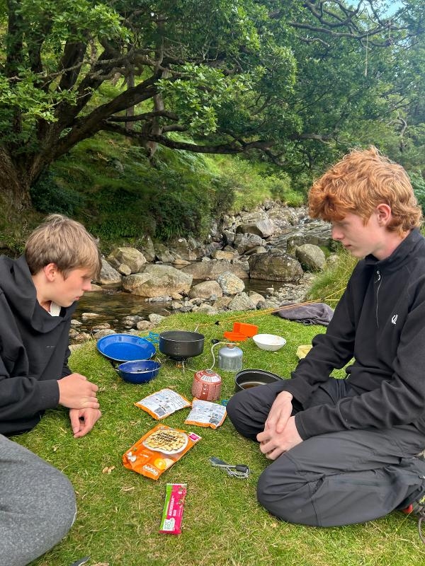 2 Jugendlichen campen in der Natur gemeinsam und kochen etwas zu Essen 