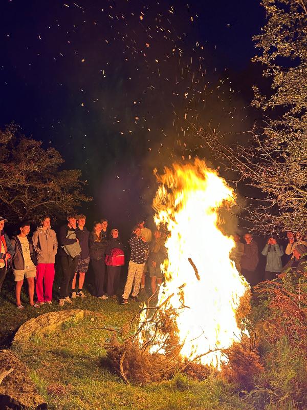 Eine große Gruppe gemeinsam um ein großes Lagerfeuer im Wald